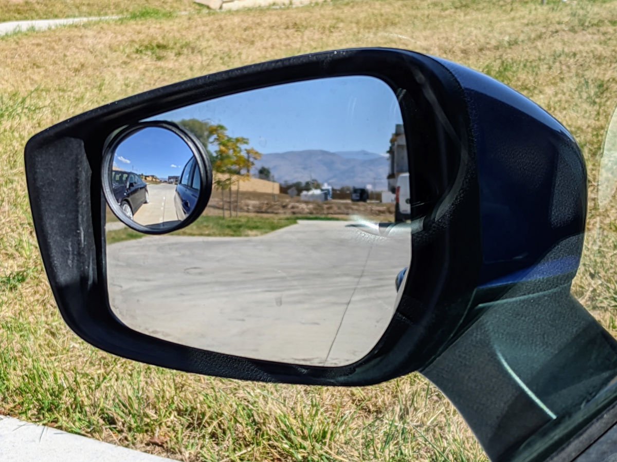 Same photo of a side view mirror but with a blind spot mirror that shows a car visible to the side