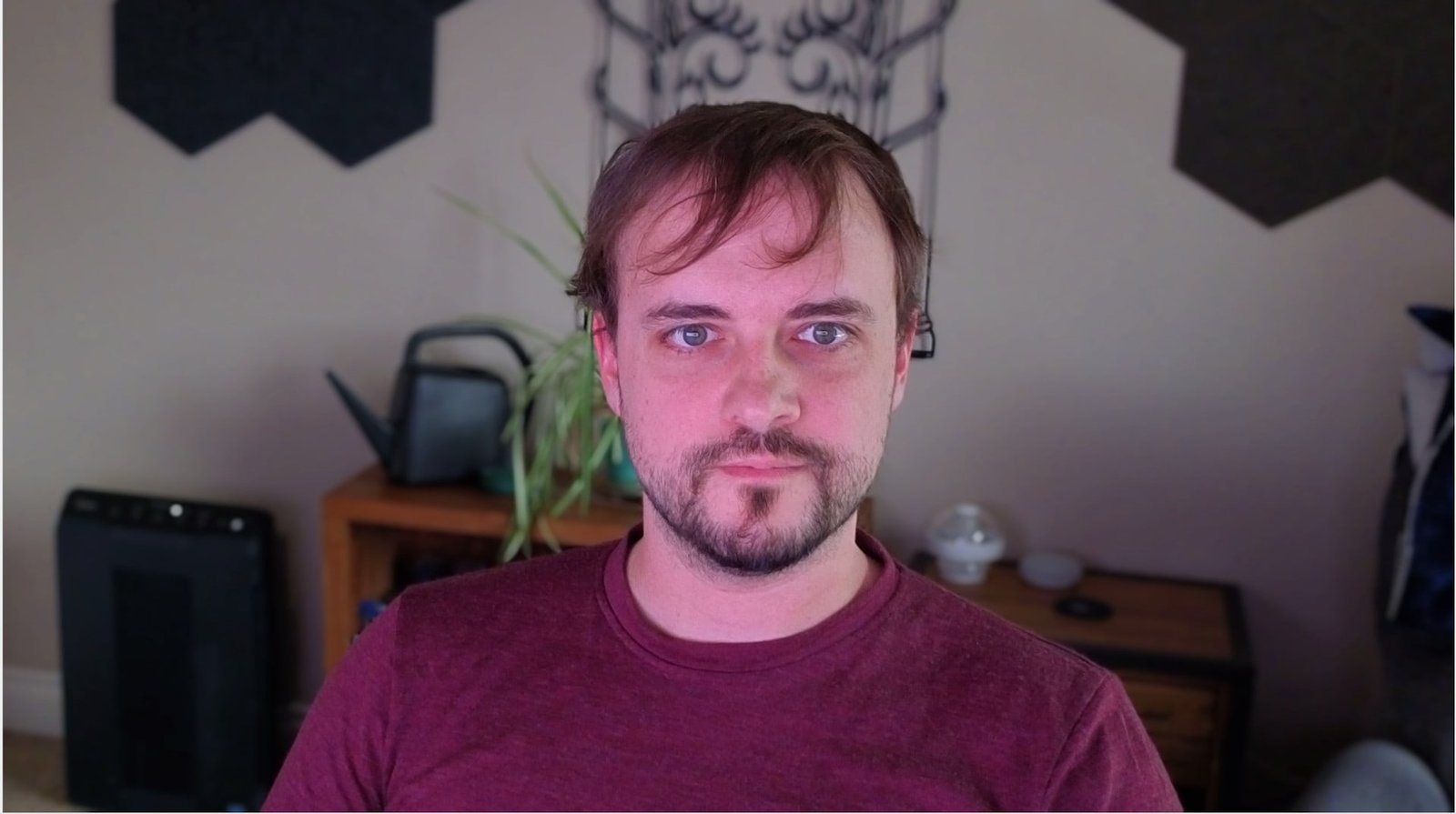 Insta360 Link webcam capture in a dark room with only dim window light. Despite poor lighting conditions, the face remains clearly visible with reasonable detail and sharpness, though skin tones show an unnatural pinkish cast. Significantly better performance than the Logitech C920 in similar low-light conditions.